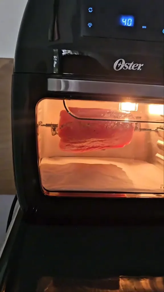 Air fryer Oster assando carne no espeto giratório com luz acesa