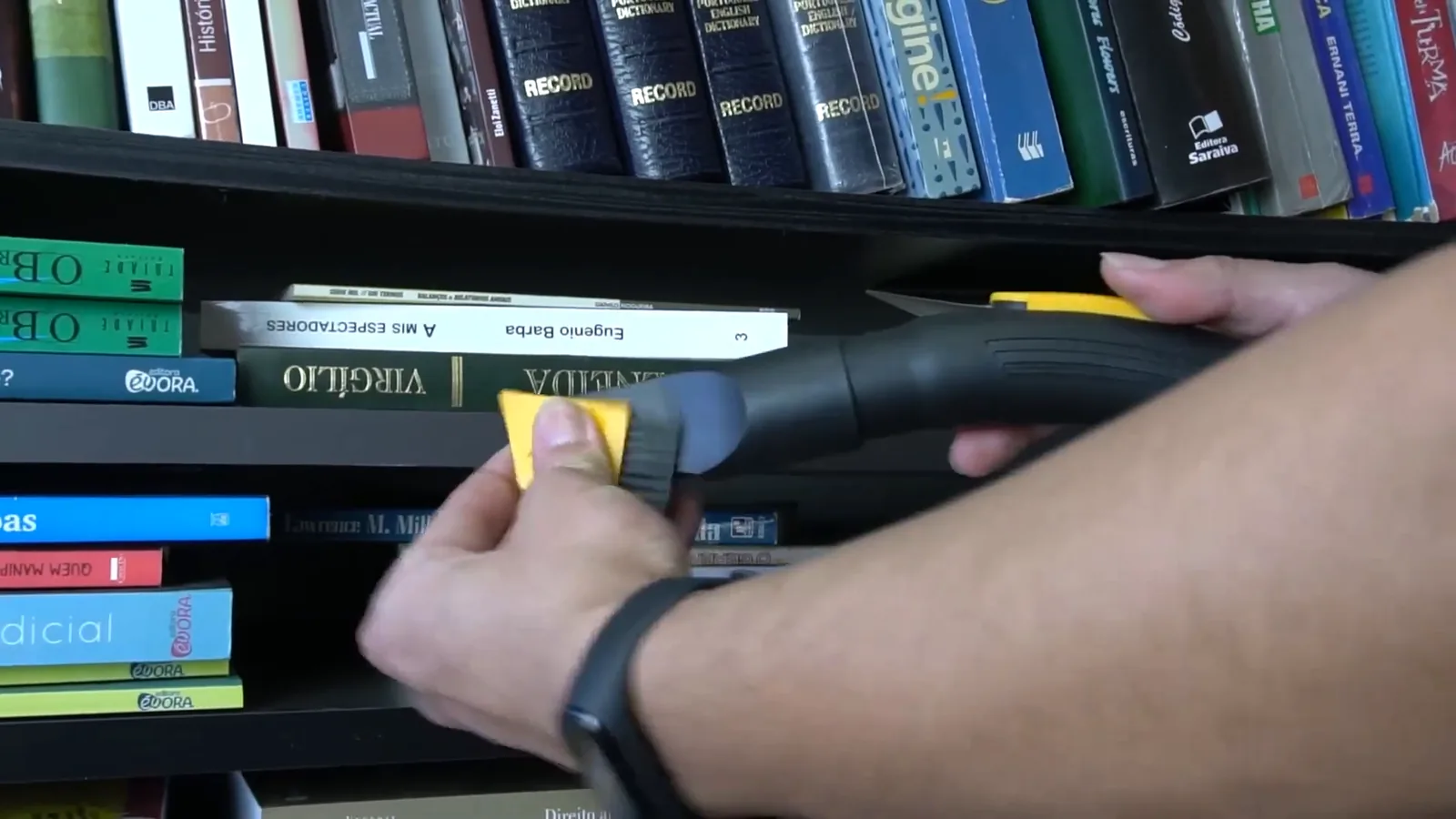 Bocal com escova limpando poeira acumulada em prateleira de livros