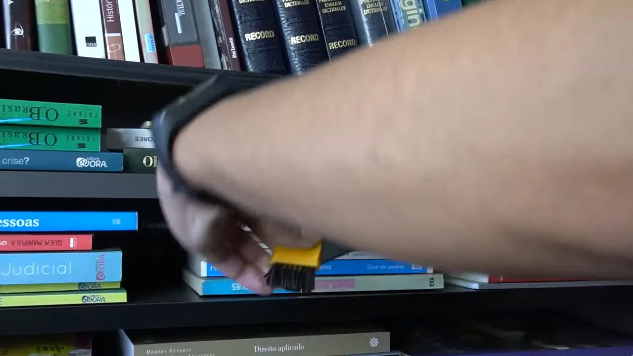 Bocal com escova sendo utilizado para limpar livros na estante