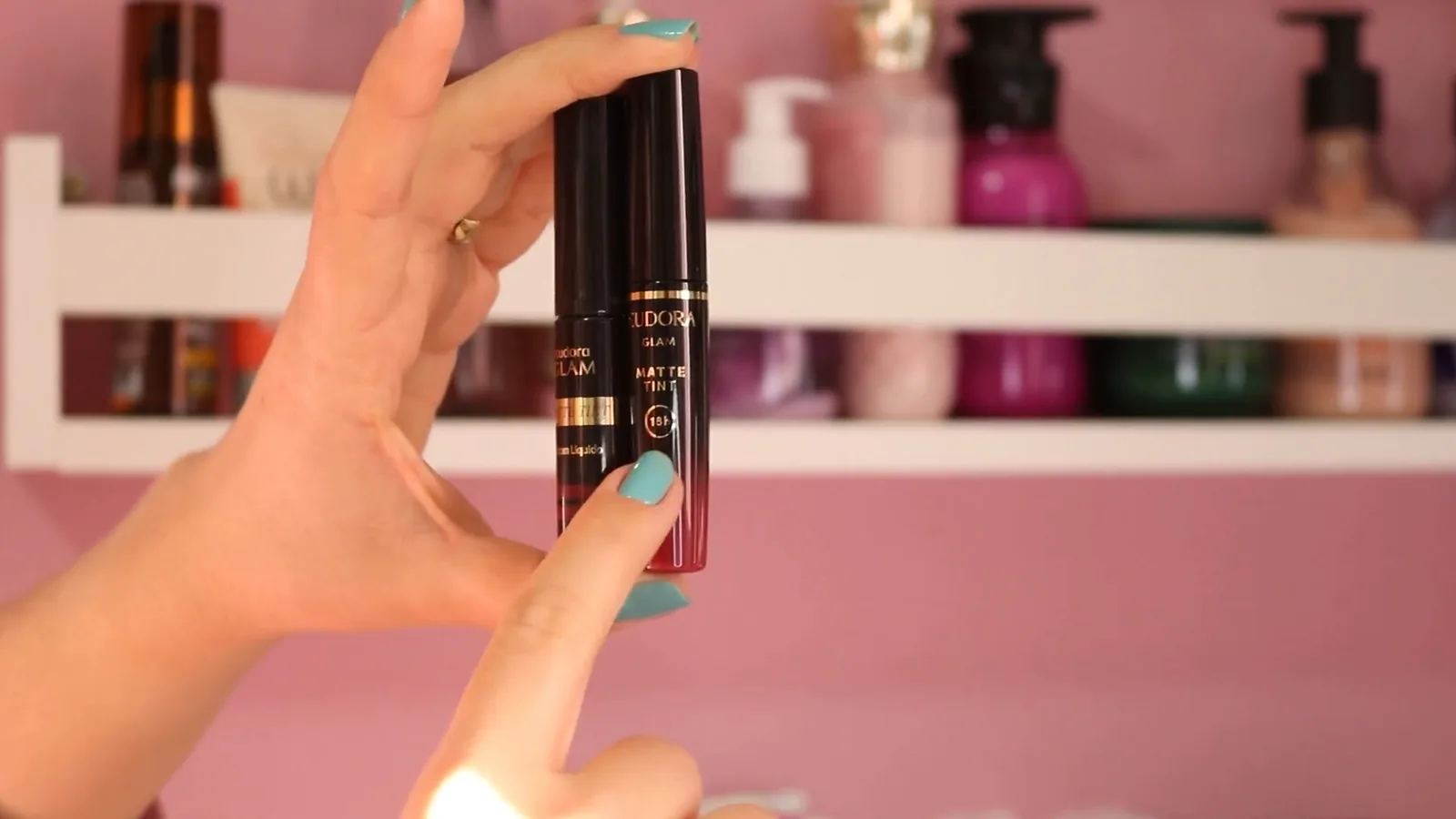 Frascos do batom líquido Eudora Glam Matte Tint segurados em mãos