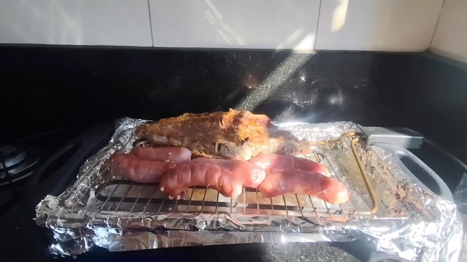 Bife dourado e linguiças assando na grelha da churrasqueira elétrica