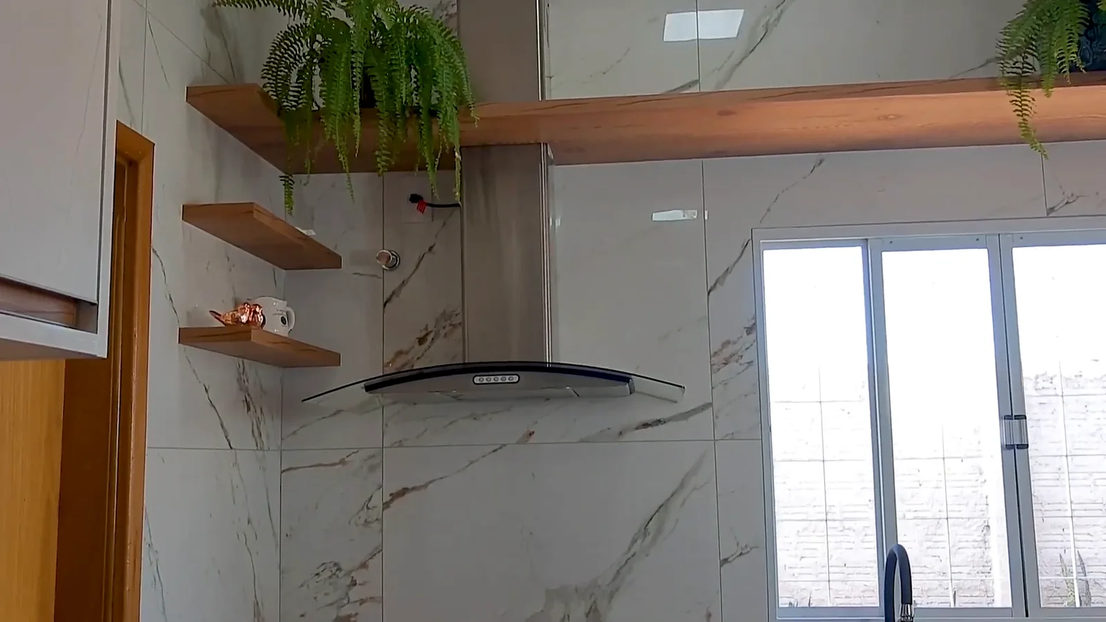 Coifa Fogatti instalada na parede marmorizada sobre bancada da cozinha