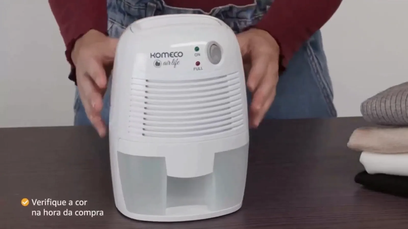 Desumidificador Komeco compacto posicionado sobre a mesa junto a roupas