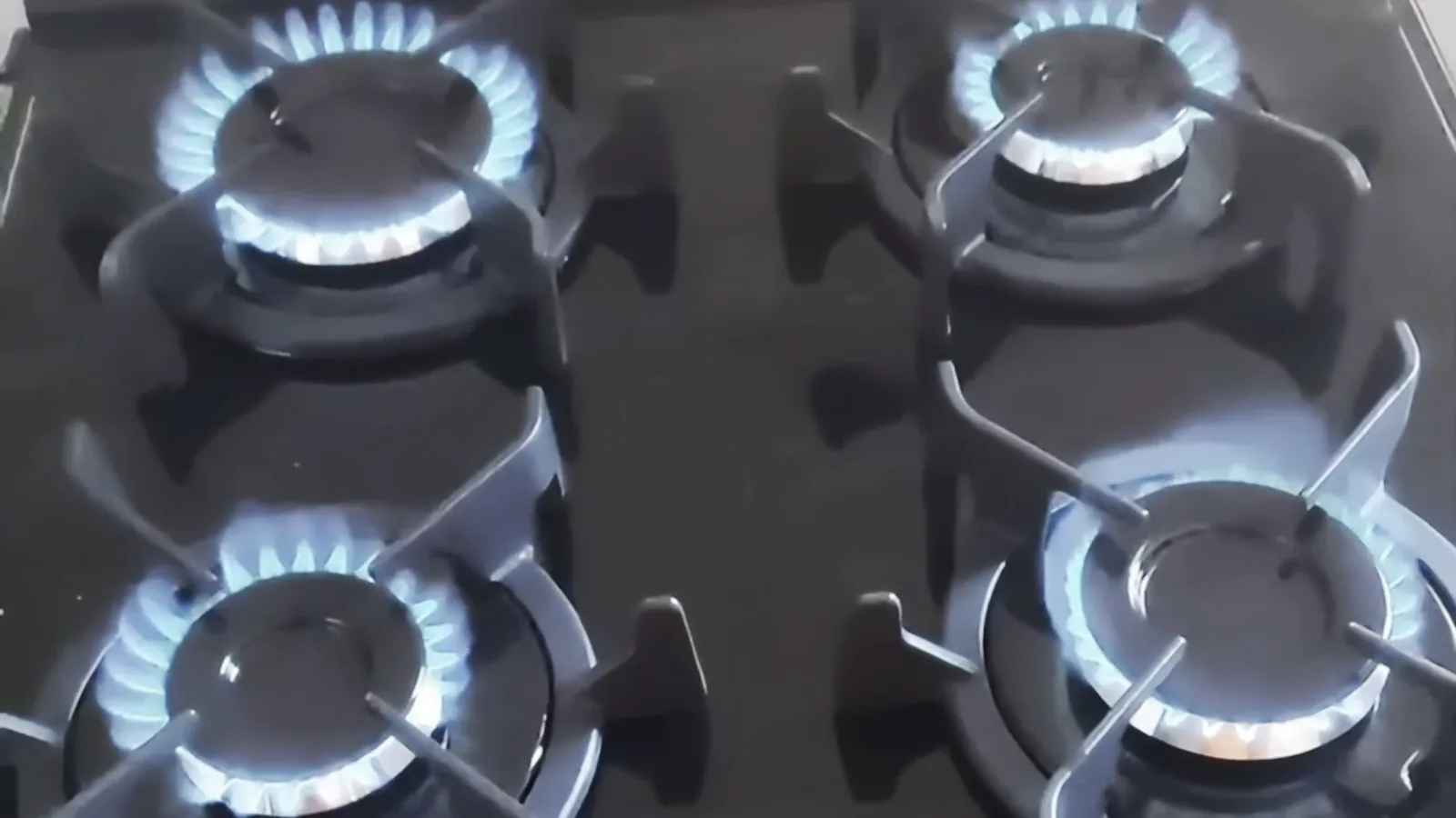 Quatro queimadores acesos com chamas azuis na mesa de vidro