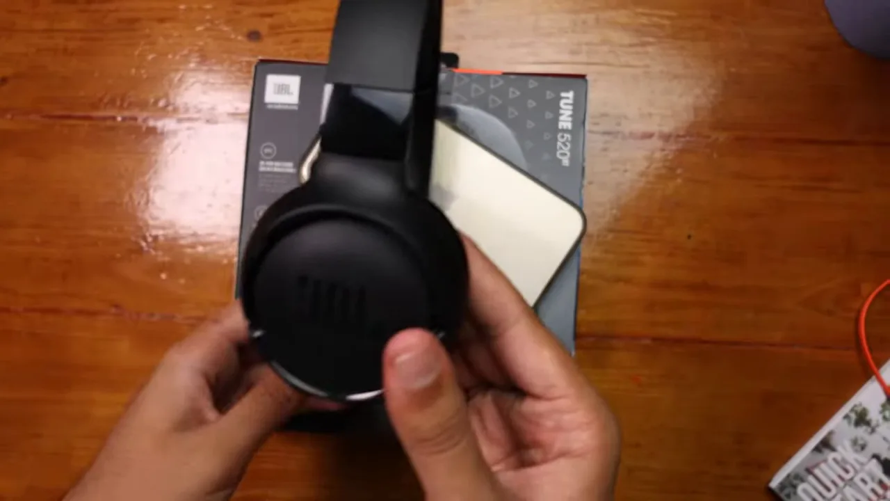 Apresentador manuseia o fone JBL Tune 520BT mostrando estrutura e conchas