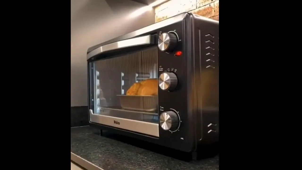 Forno elétrico ligado na bancada preparando frango assado com douramento