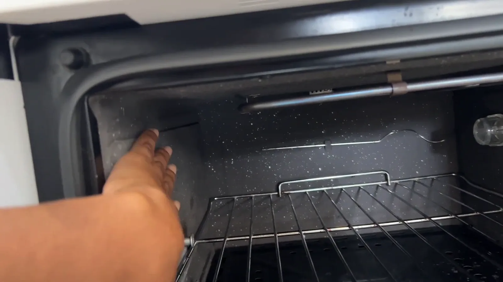 Mão apontando o revestimento autolimpante nas paredes internas do forno