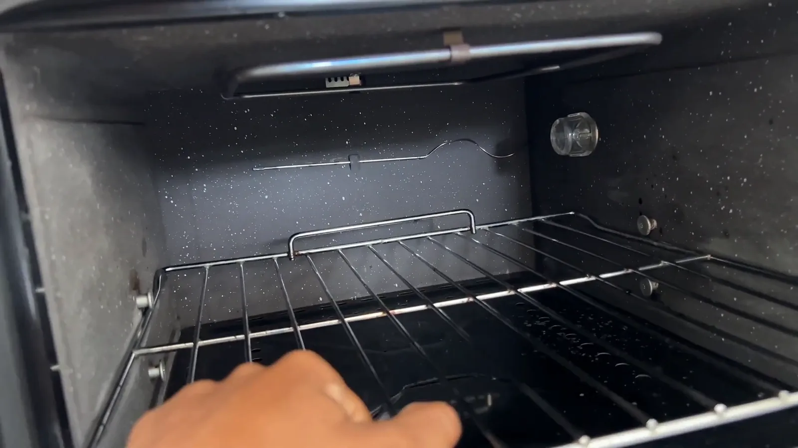 Grelha metálica sendo ajustada nos trilhos internos do forno elétrico