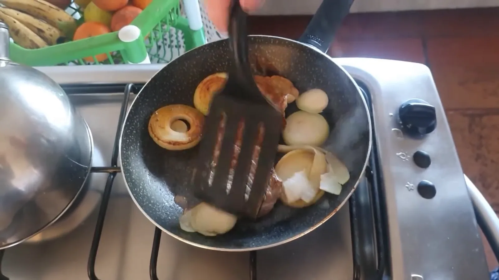 Bife e rodelas de cebola dourando na frigideira antiaderente Rochedo