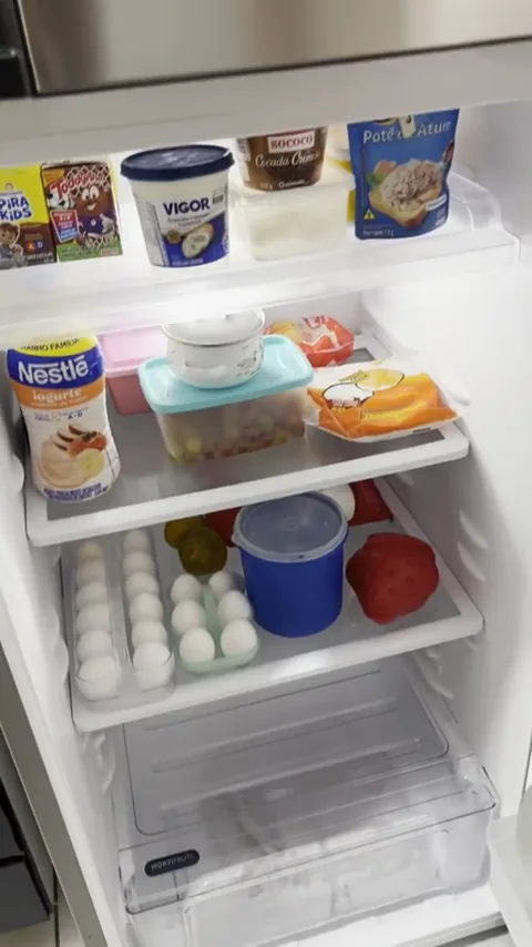 Compartimento refrigerador interno com prateleiras ocupadas e gaveta de legumes
