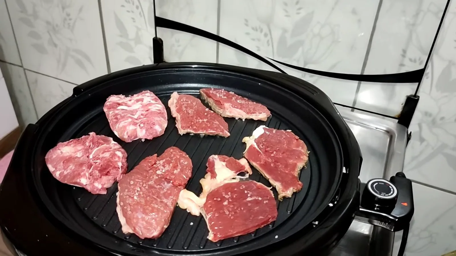 Vários pedaços de carne grelhando na ampla chapa redonda do aparelho