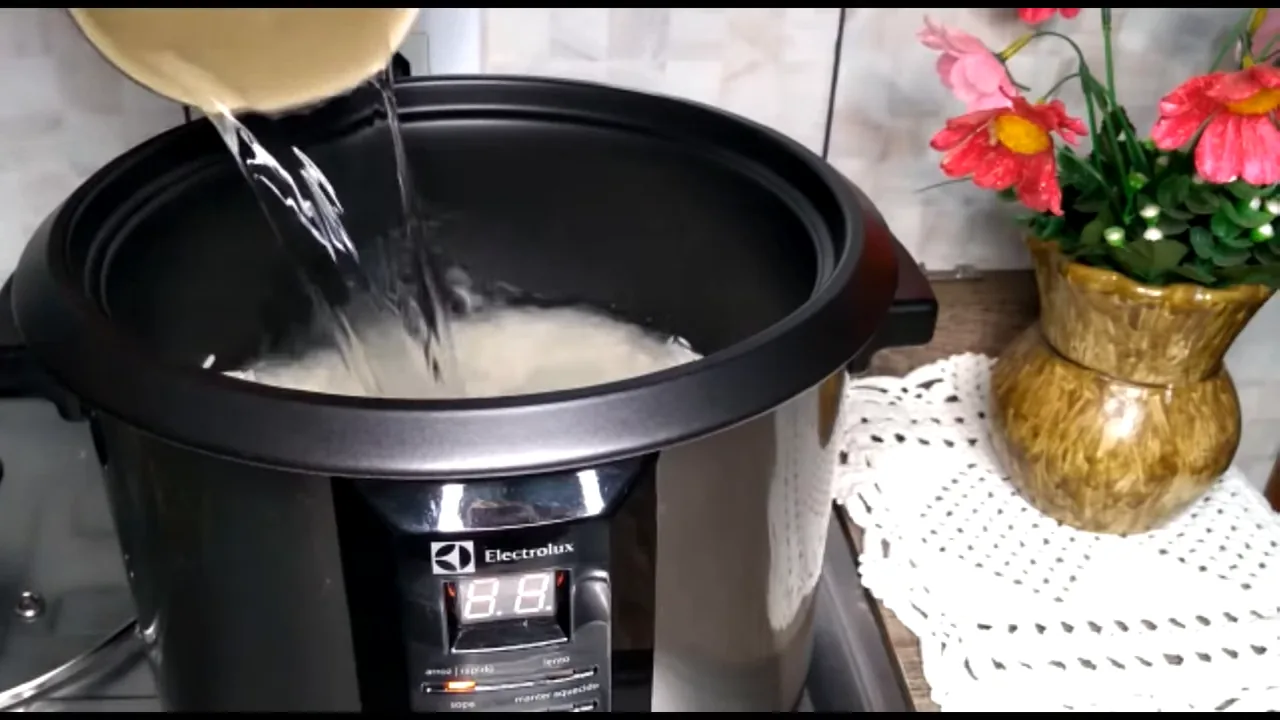 Despejando água no arroz para cozimento na panela elétrica