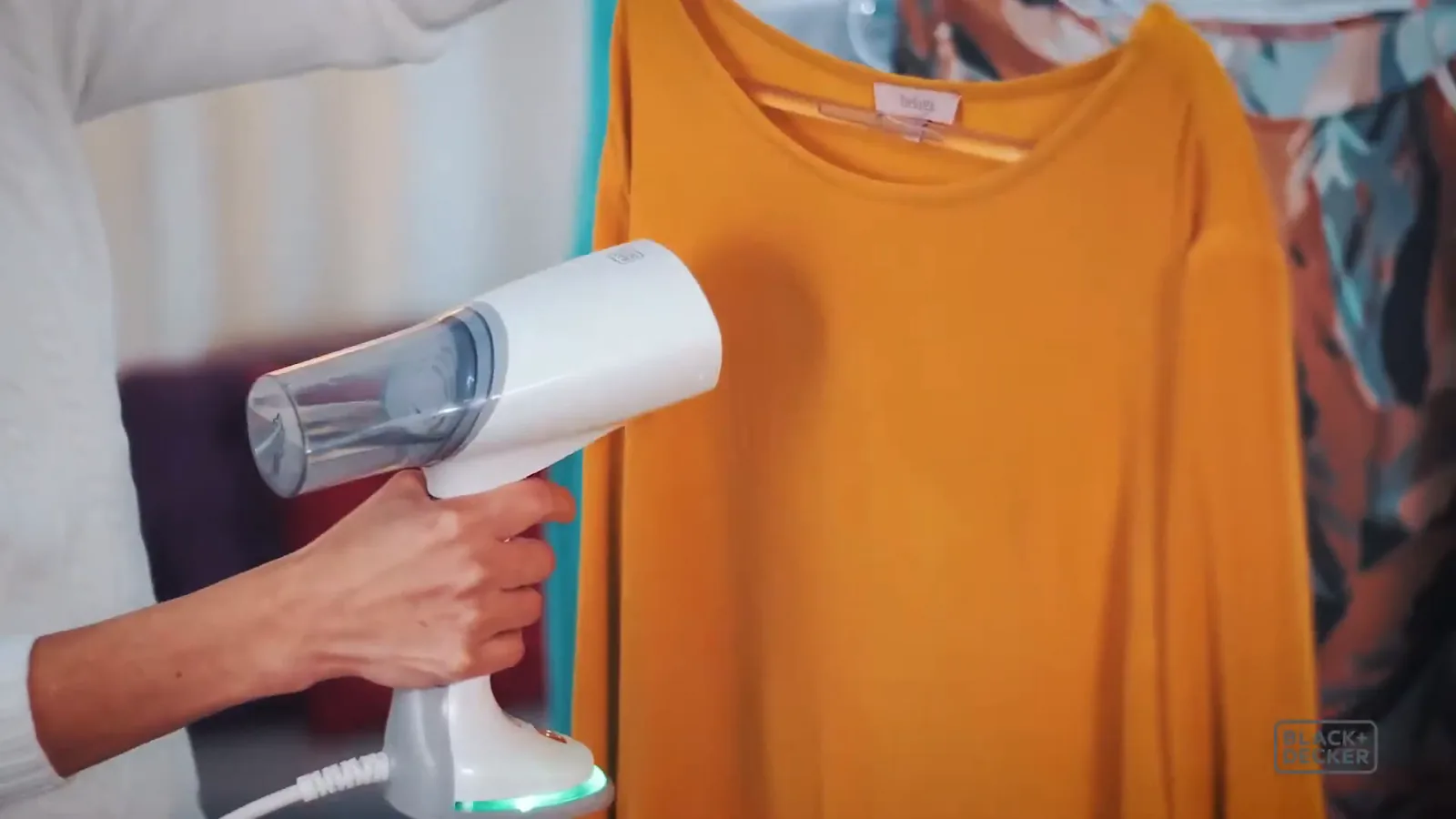 Passadeira a vapor desamassando camisa amarela pendurada no cabide