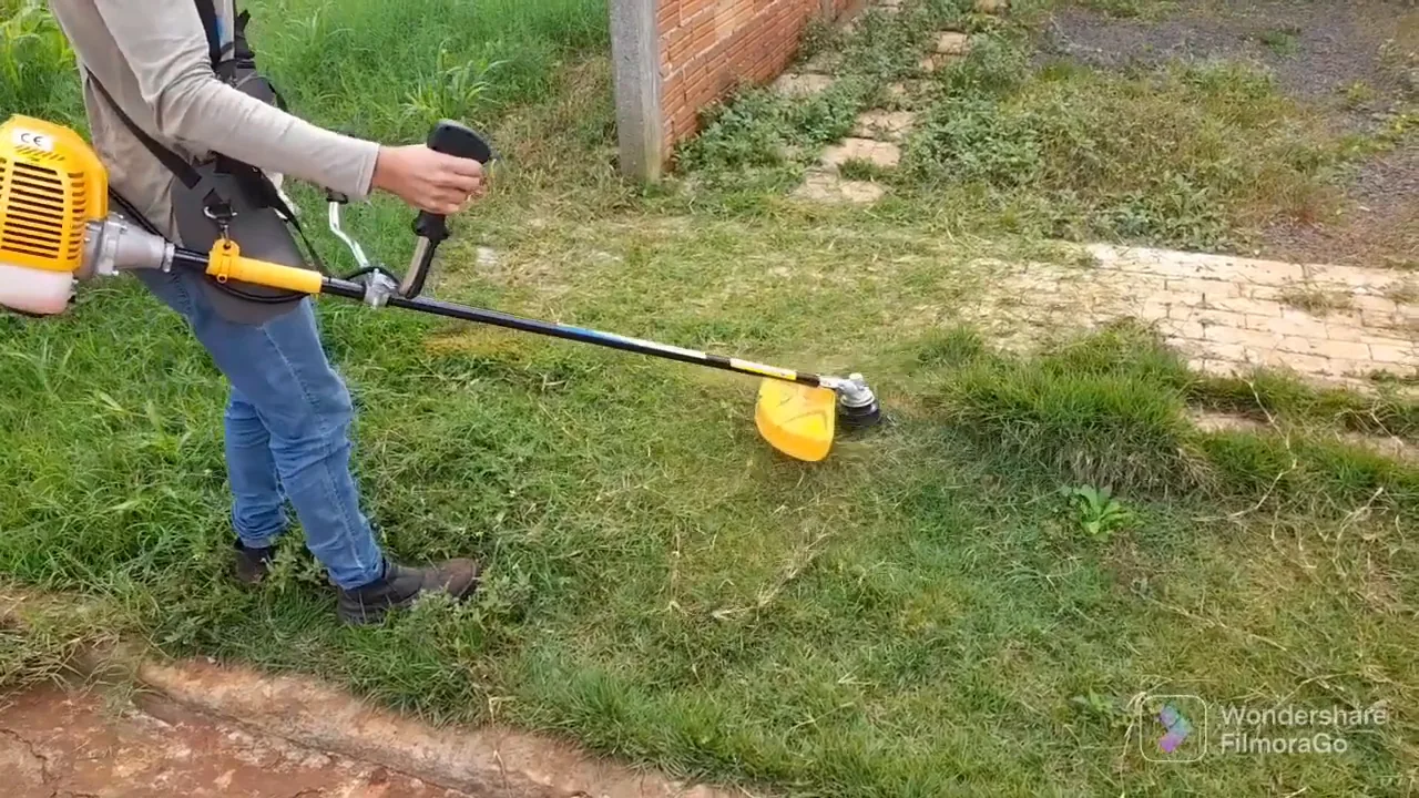 Roçadeira a gasolina aparando gramado próximo à calçada