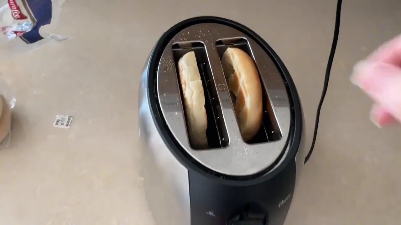 Fatia de pão bagel tostada sendo retirada da torradeira Oster