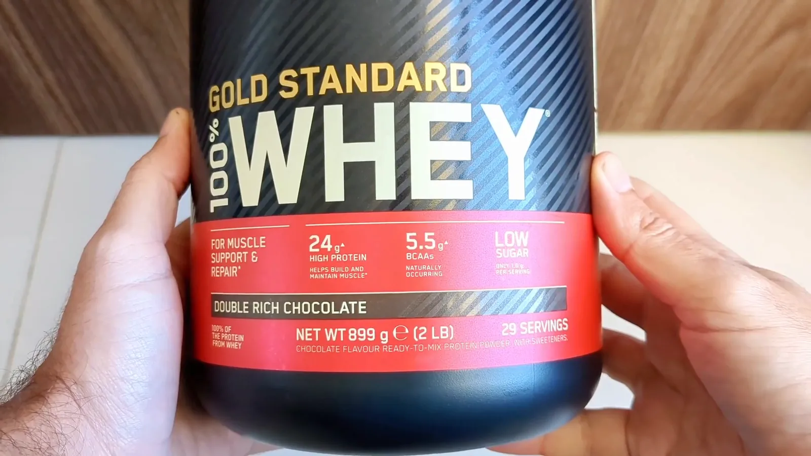 Pote de whey protein Gold Standard da Optimum Nutrition em mãos